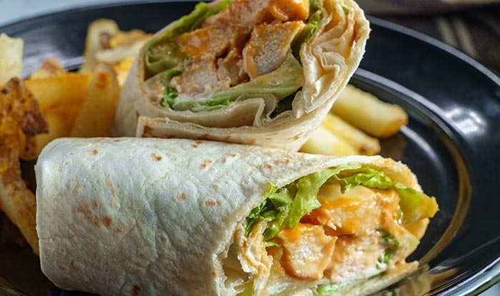 Two chicken wraps with lettuce and fries—a perfect Sports Bar food favorite on a black plate.