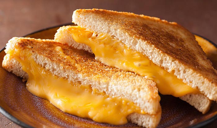 Two halves of a grilled cheese from Bricks & Ivy Tavern, melted cheese oozing on a brown plate.