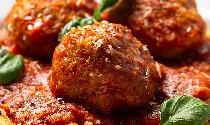A close-up of meatballs in tomato sauce at Bricks & Ivy Restaurant, garnished with basil leaves.