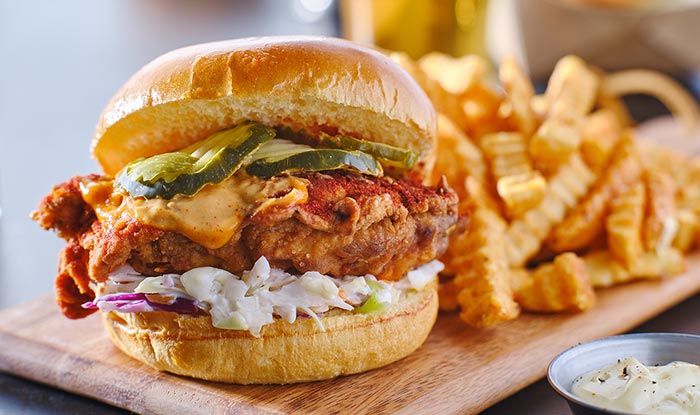 Crispy chicken sandwich with pickles and fries, served tavern-style on a wooden board.
