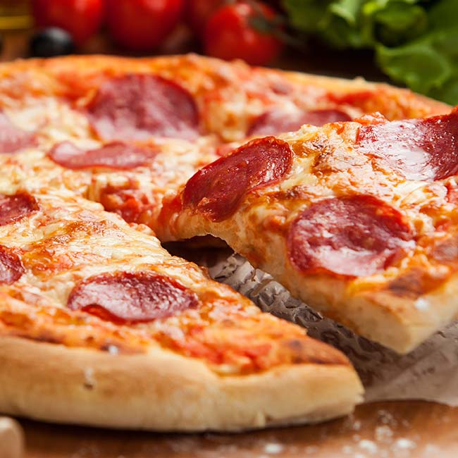 A pepperoni pizza from Bricks & Ivy with a slice lifted, served on a wooden surface.