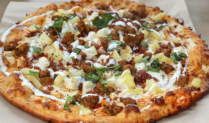 Bricks & Ivy Tavern food: Pizza with sausage, pineapple, herbs, and white sauce on parchment.