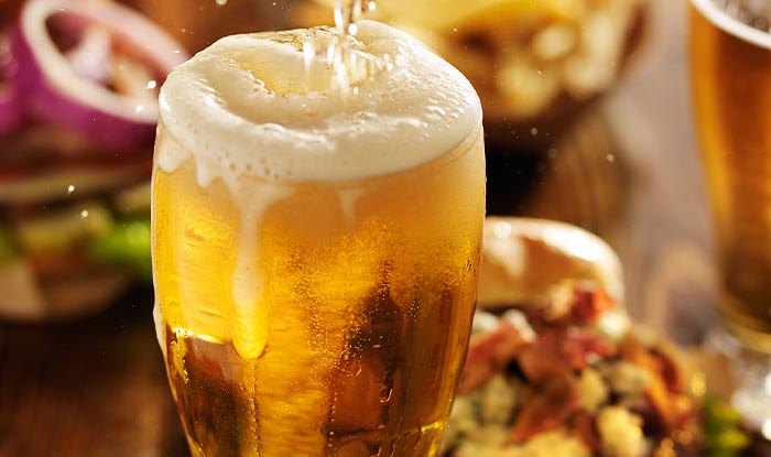 A glass of beer overflows with foam at Bricks & Ivy tavern, food blurred in the background.