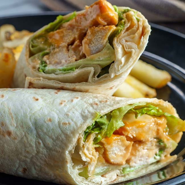 Chicken wrap with lettuce and sauce, sliced in half, served with fries at Bricks & Ivy Tavern.